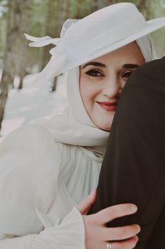 A joyful bride in a hijab embraces her groom in a serene snowy forest during a winter wedding.