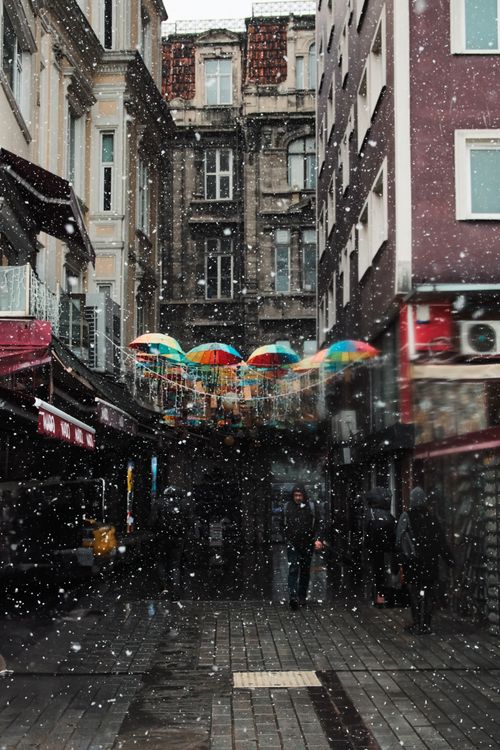 Free A vibrant urban street adorned with colorful umbrellas during a snowy day. Stock Photo