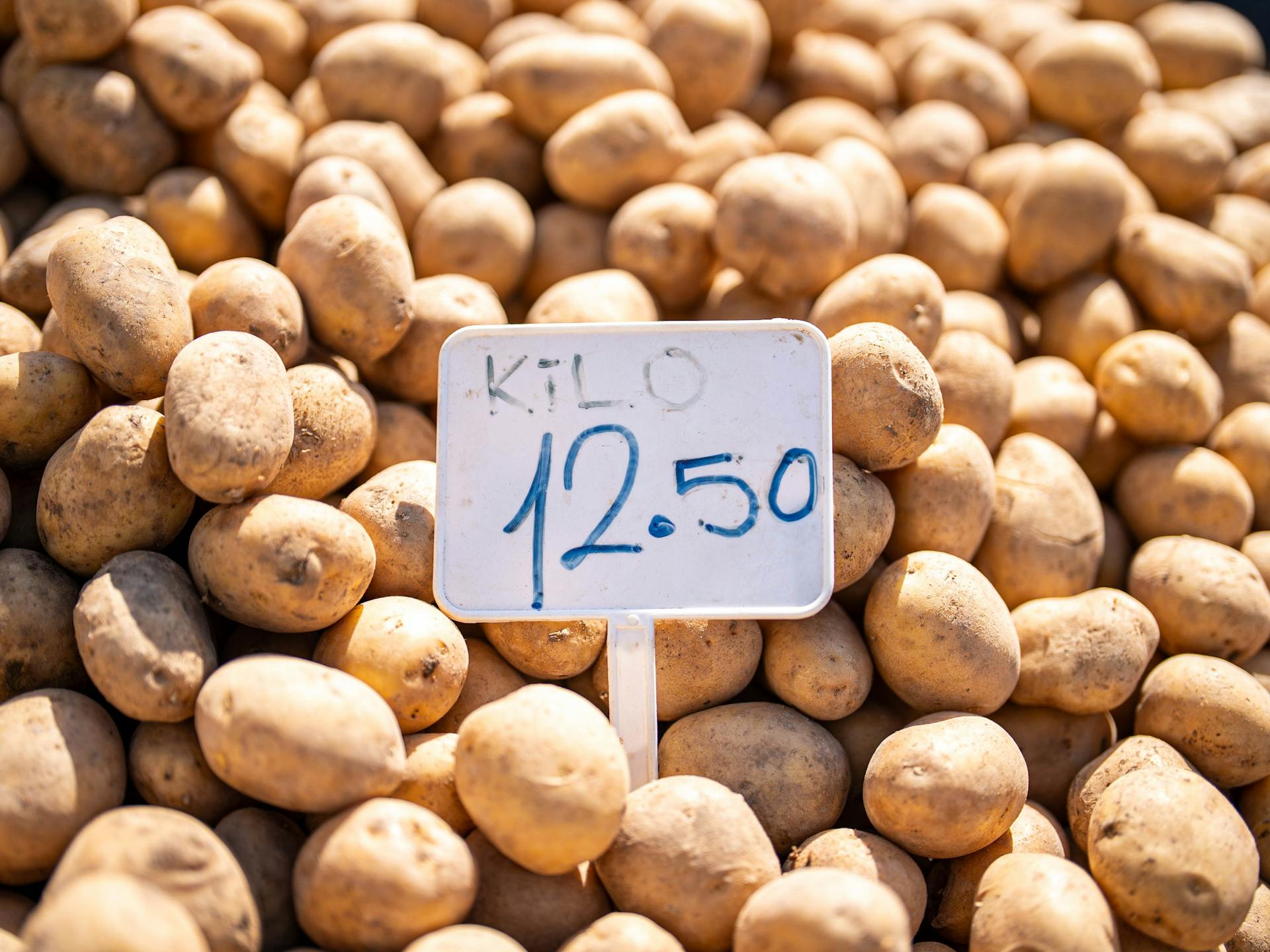 Close-up of fresh potatoes at a market with a price tag displaying 12.50 per kilo.