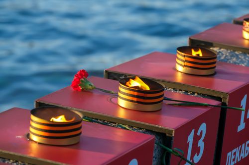 Free Flame-lit memorial setup with a red carnation by the water, reflecting memorial atmosphere. Stock Photo