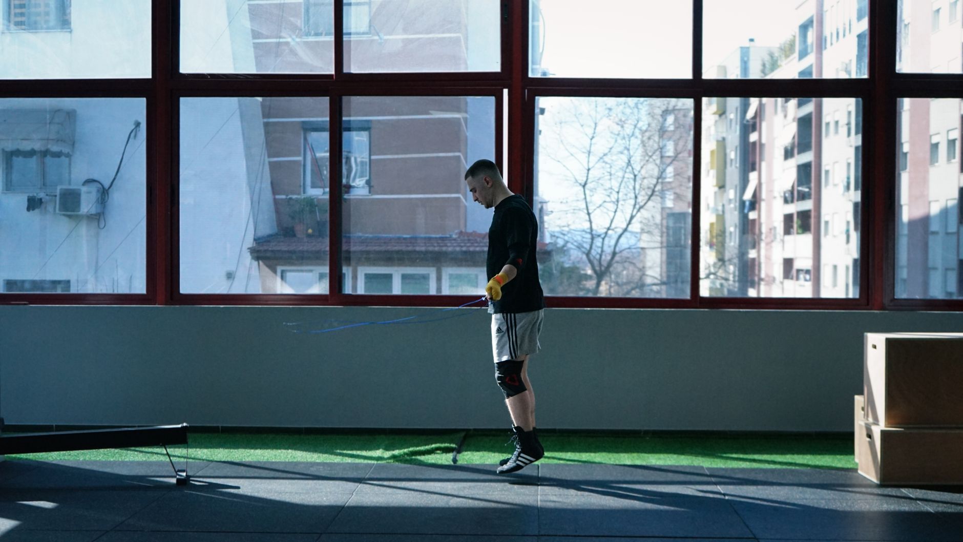 Young man exercising with a skipping rope in an urban gym with large windows and city view.