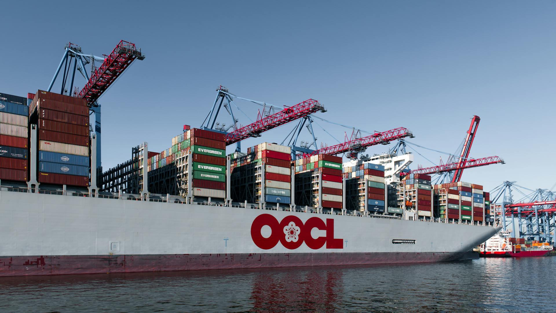Massive cargo ship loaded with containers at Hamburg port under clear blue sky.