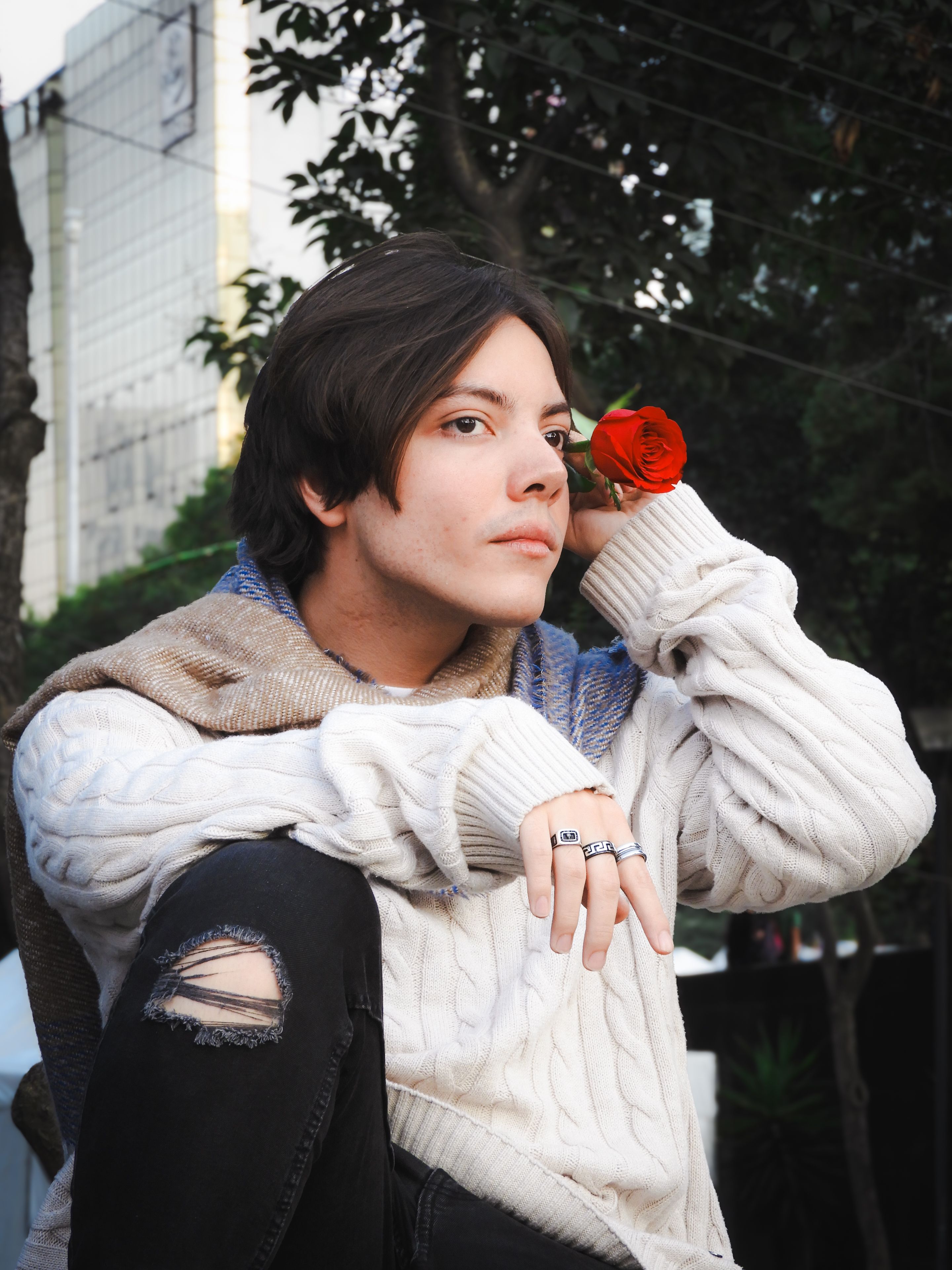 Young man in contemplative pose holding a red rose outdoors in Mexico City. Urban setting.