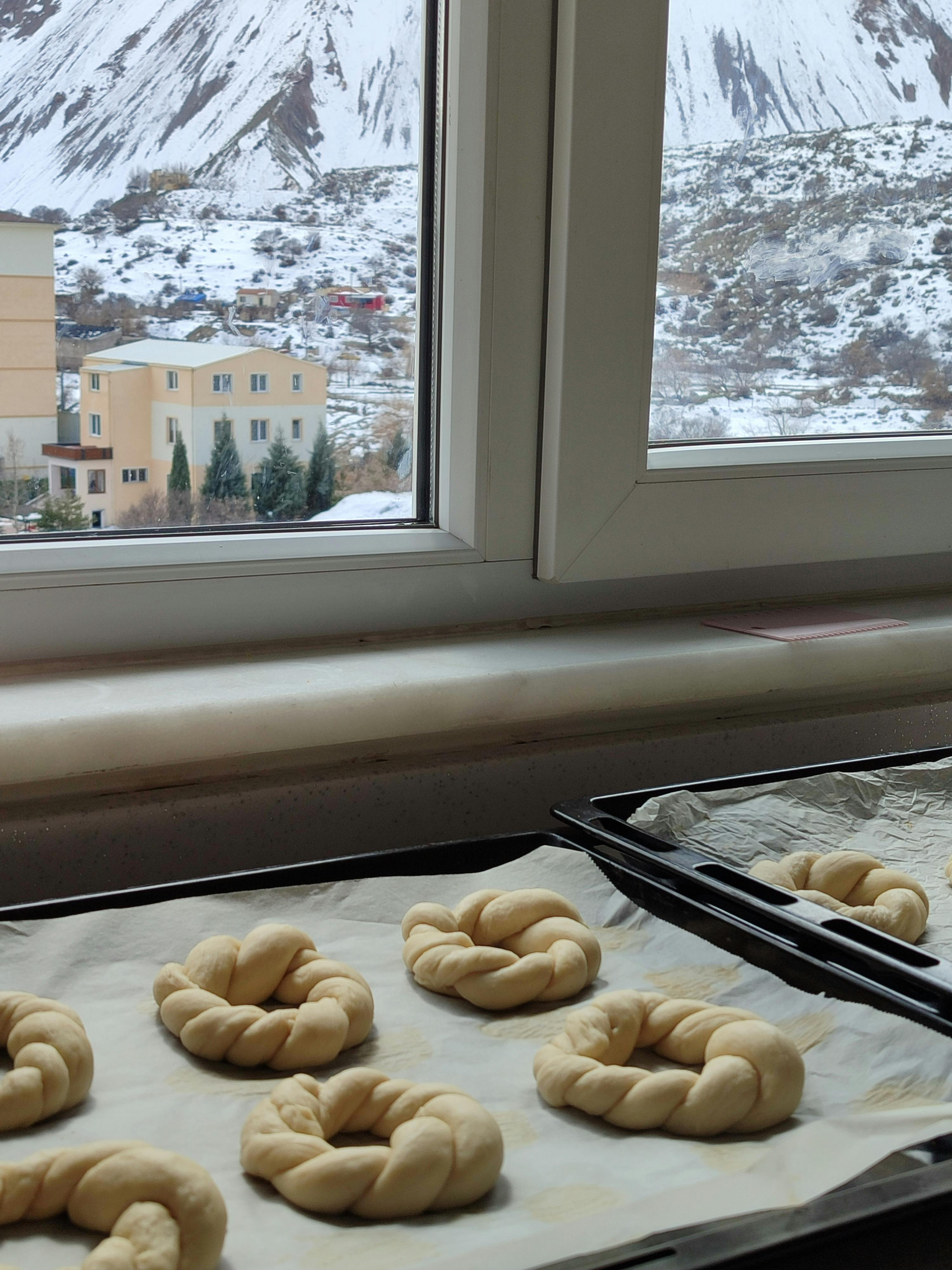 Fresh twisted bread dough on tray by snowy mountain view through window.