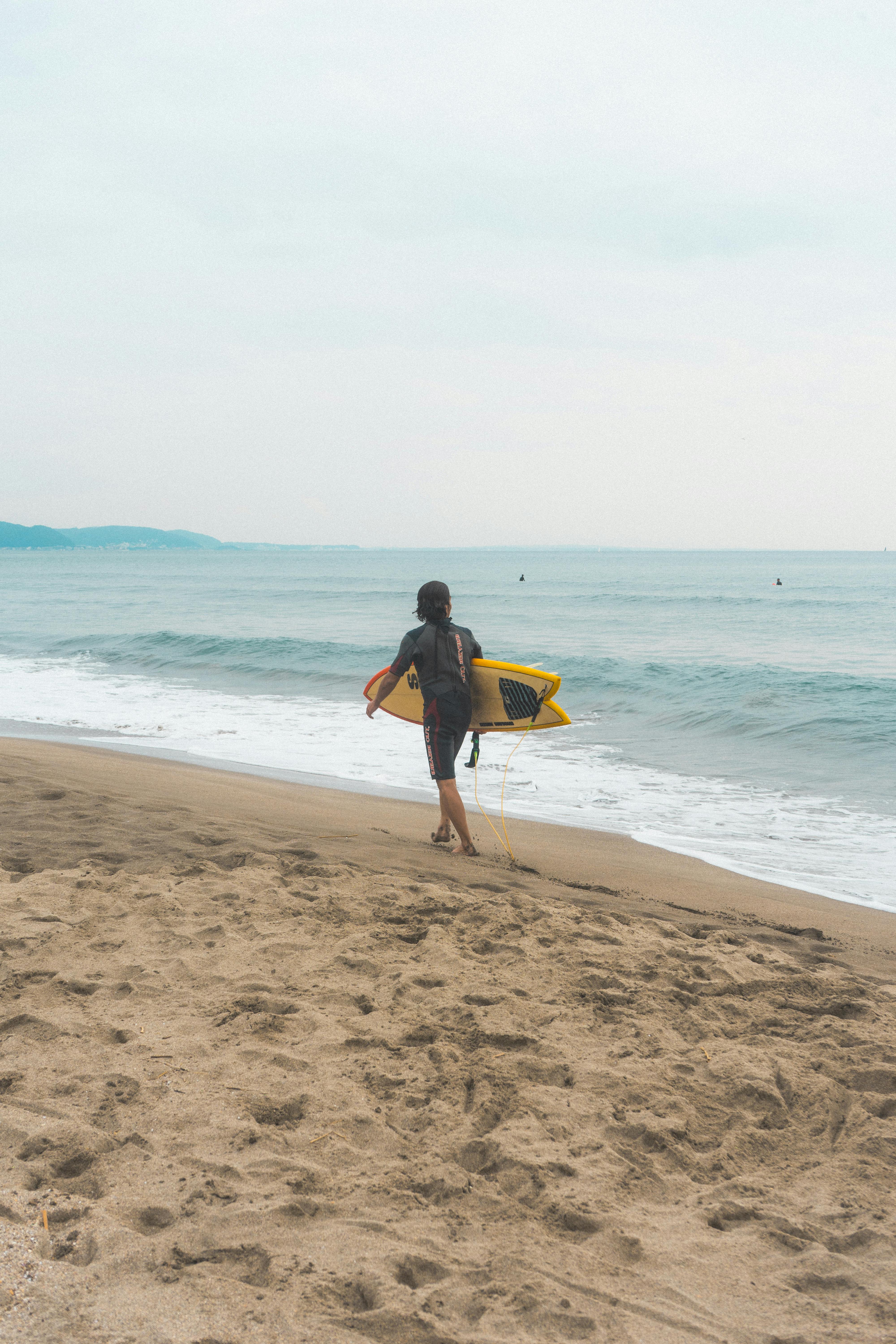 A surfer walks along Kamakura Beach in Japan, readying for the waves.