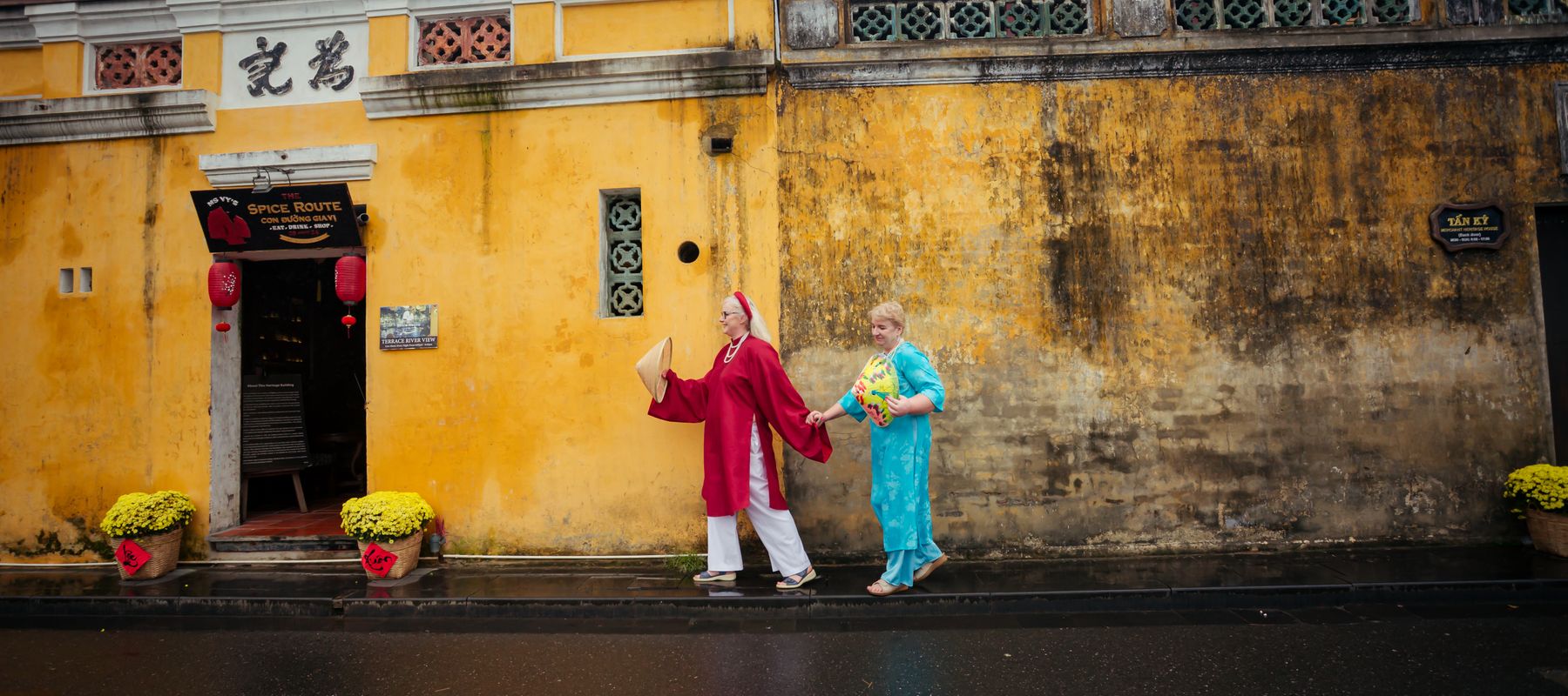 A couple in traditional attire walking in front of Hội An's historic yellow walls.