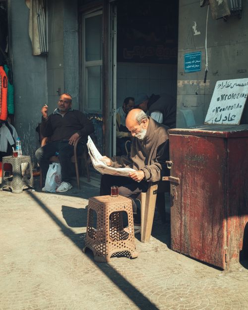 Free Elderly man reads newspaper outside a café, reflecting everyday Middle Eastern life. Stock Photo
