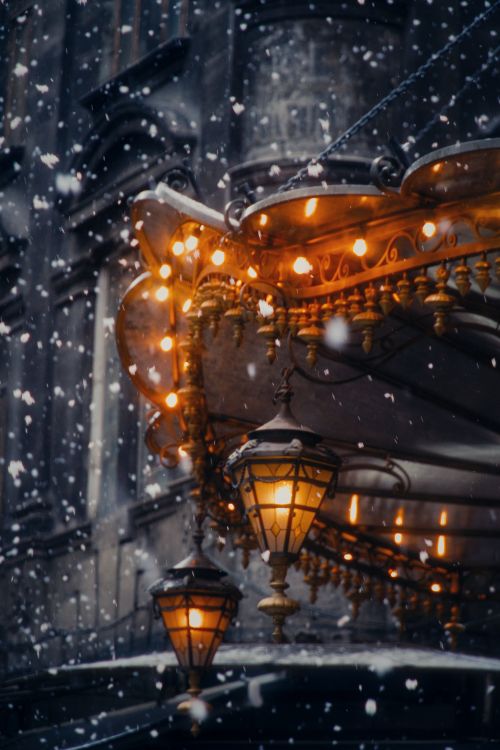 Free Vintage lanterns glow warmly amidst falling snowflakes on a winter street corner. Stock Photo