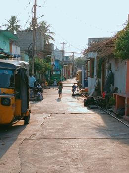 Street view of a vibrant Indian neighborhood with auto rickshaw and children playing.