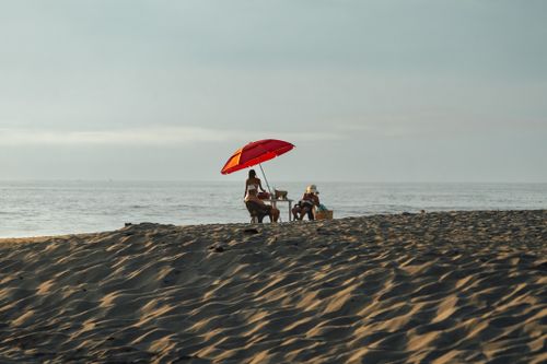 Free Peaceful beach scene in Oaxaca, Mexico with people relaxing under a vibrant red umbrella by the ocean. Stock Photo