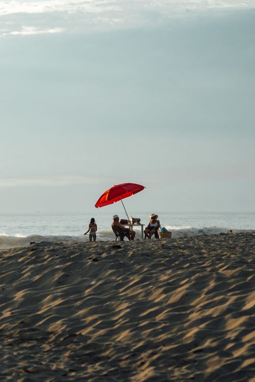 Free Beach scene in Oaxaca, Mexico featuring a red umbrella and people enjoying a sunny day. Stock Photo