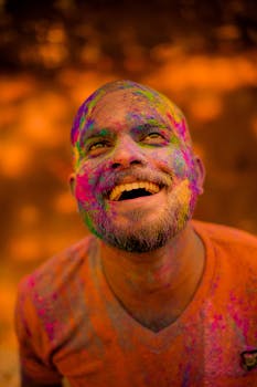 A smiling man covered in vibrant colors celebrates the traditional Holi festival in India.