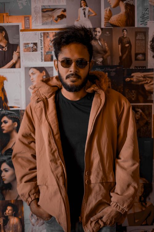 Free Young man with sunglasses and jacket standing in front of a fashion-themed wall. Stock Photo