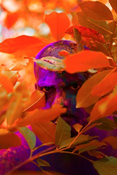 一幅充满活力的男子肖像，脸上涂着油彩，在引人注目的场景中被五颜六色的树叶环绕