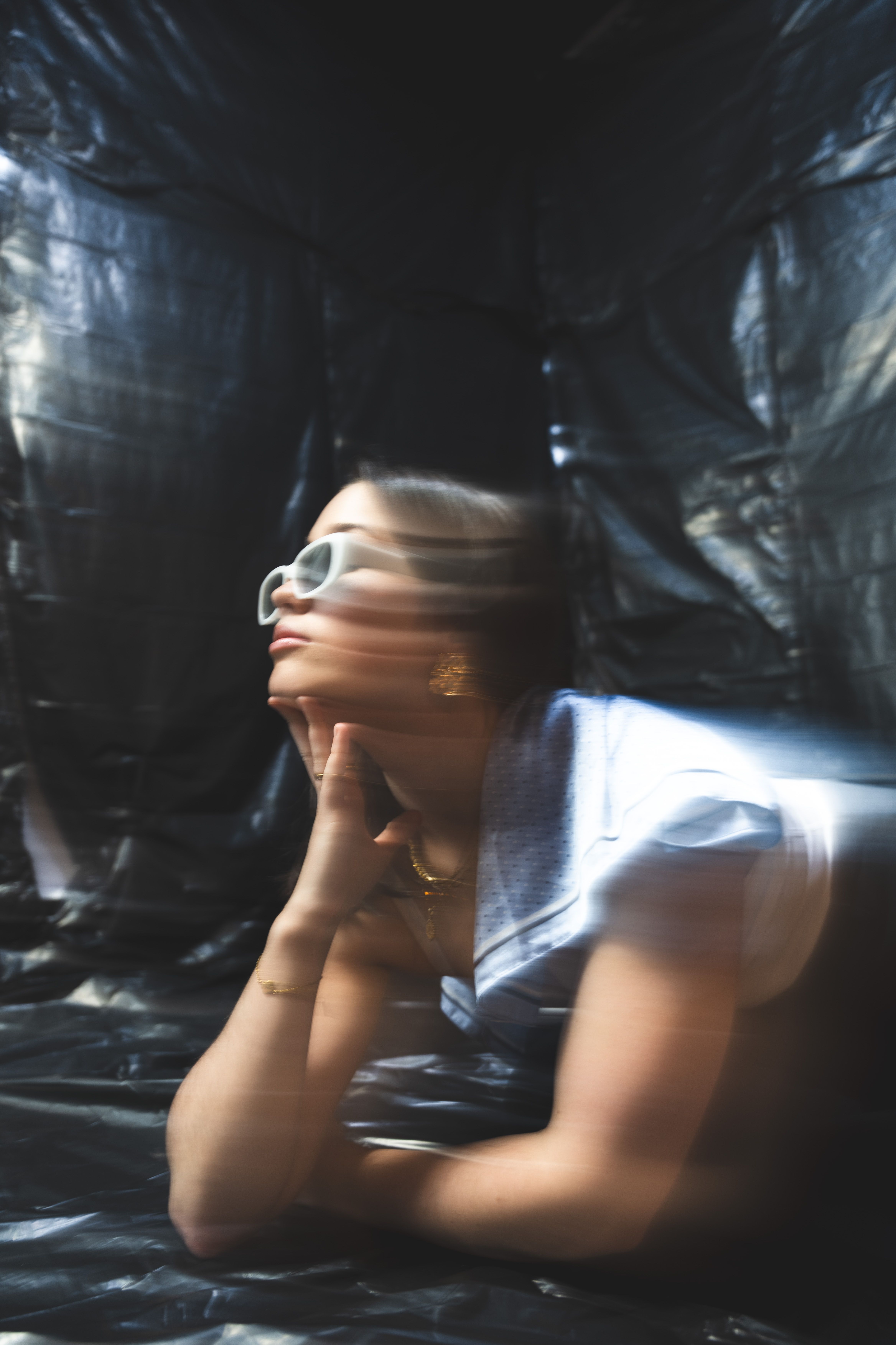 Artistic portrait of a woman with sunglasses, captured with motion blur in a studio setting.