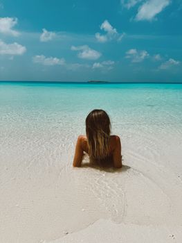 Woman enjoying a serene moment on a tropical beach with clear blue waters and white sand.