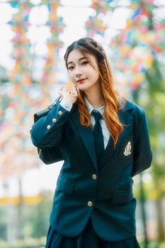 Confident young woman in school uniform with colorful backdrop outdoors.