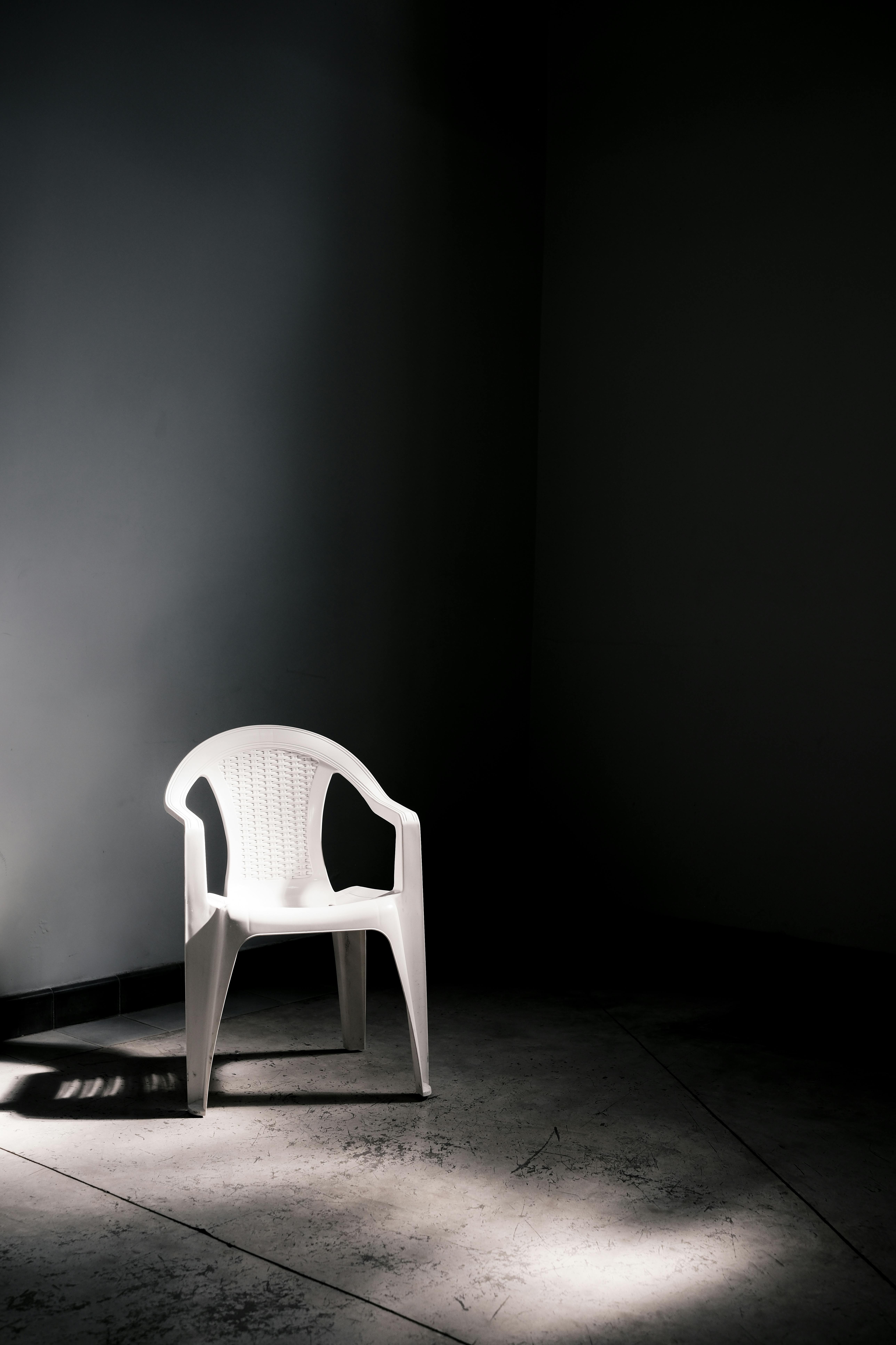A single white plastic chair illuminated by soft light in a dark, minimalist room.