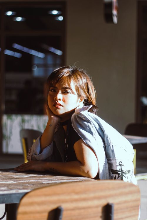 Free A woman in a denim jacket sits at a café table, enjoying the sunlight. Stock Photo