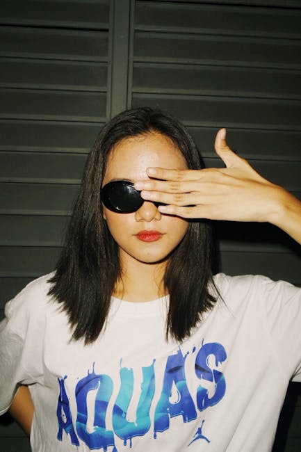 Young woman wearing sunglasses and white shirt with text, posing confidently.
