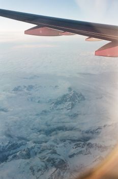 Snowy mountain landscape viewed from an airplane window, showcasing the serene beauty of nature.