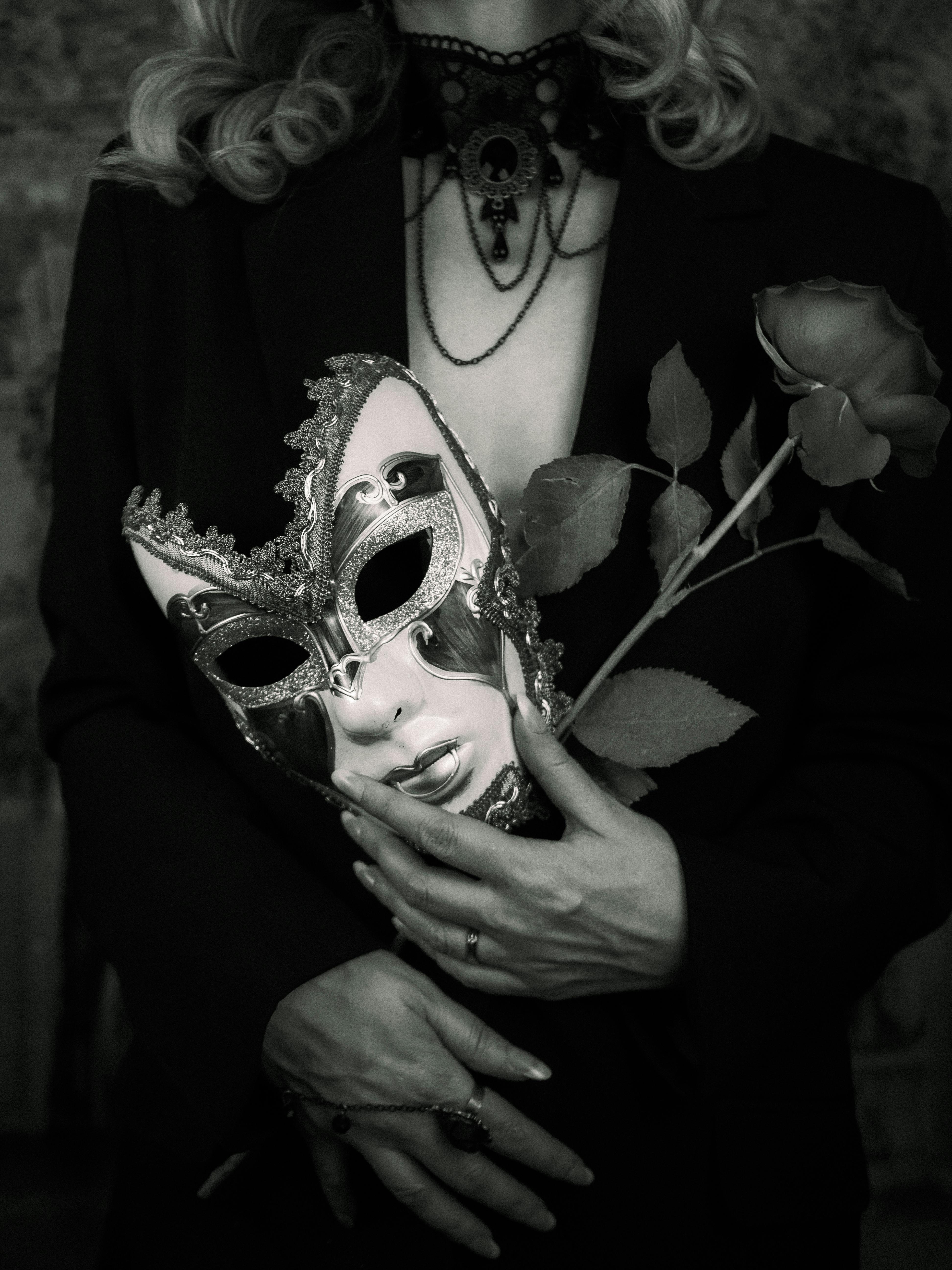 Mysterious woman holding a venetian mask and rose, dressed in gothic style.