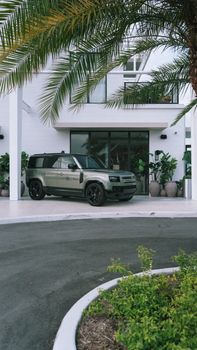 Stylish SUV parked outside a modern minimalist house with tropical plants.