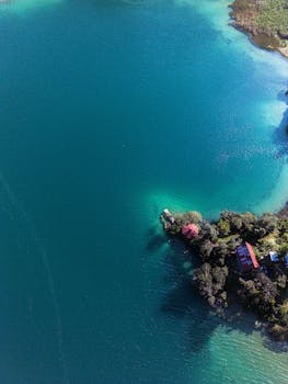 Stunning aerial shot of a turquoise lake shoreline in Mexico with lush greenery and a red-roofed building.