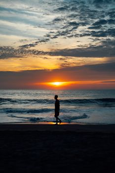 A lone figure walks along Puerto Escondido beach at sunset, creating a serene silhouette against the ocean.
