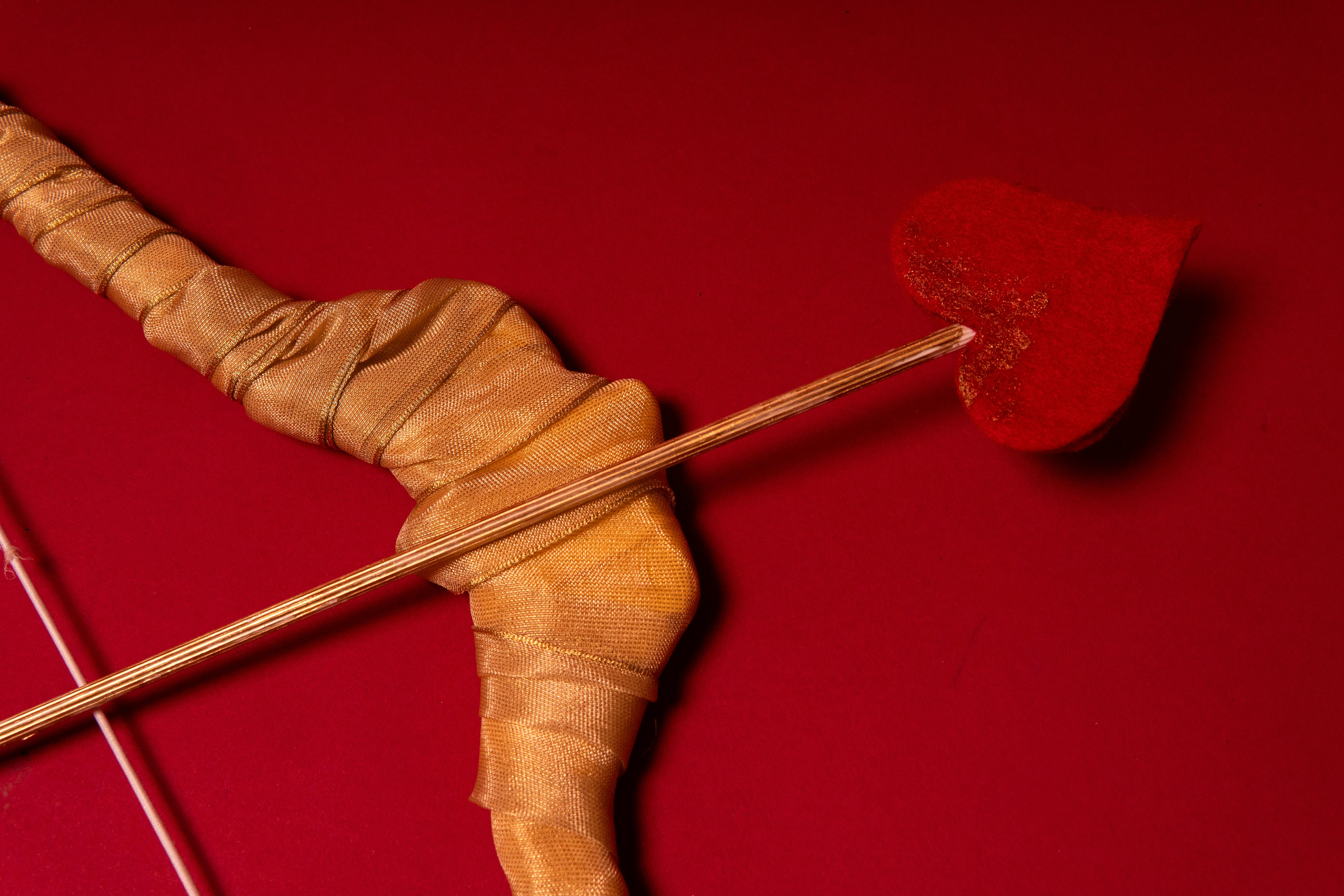 Artistic representation of a cupid's bow and arrow with a heart on a red background.