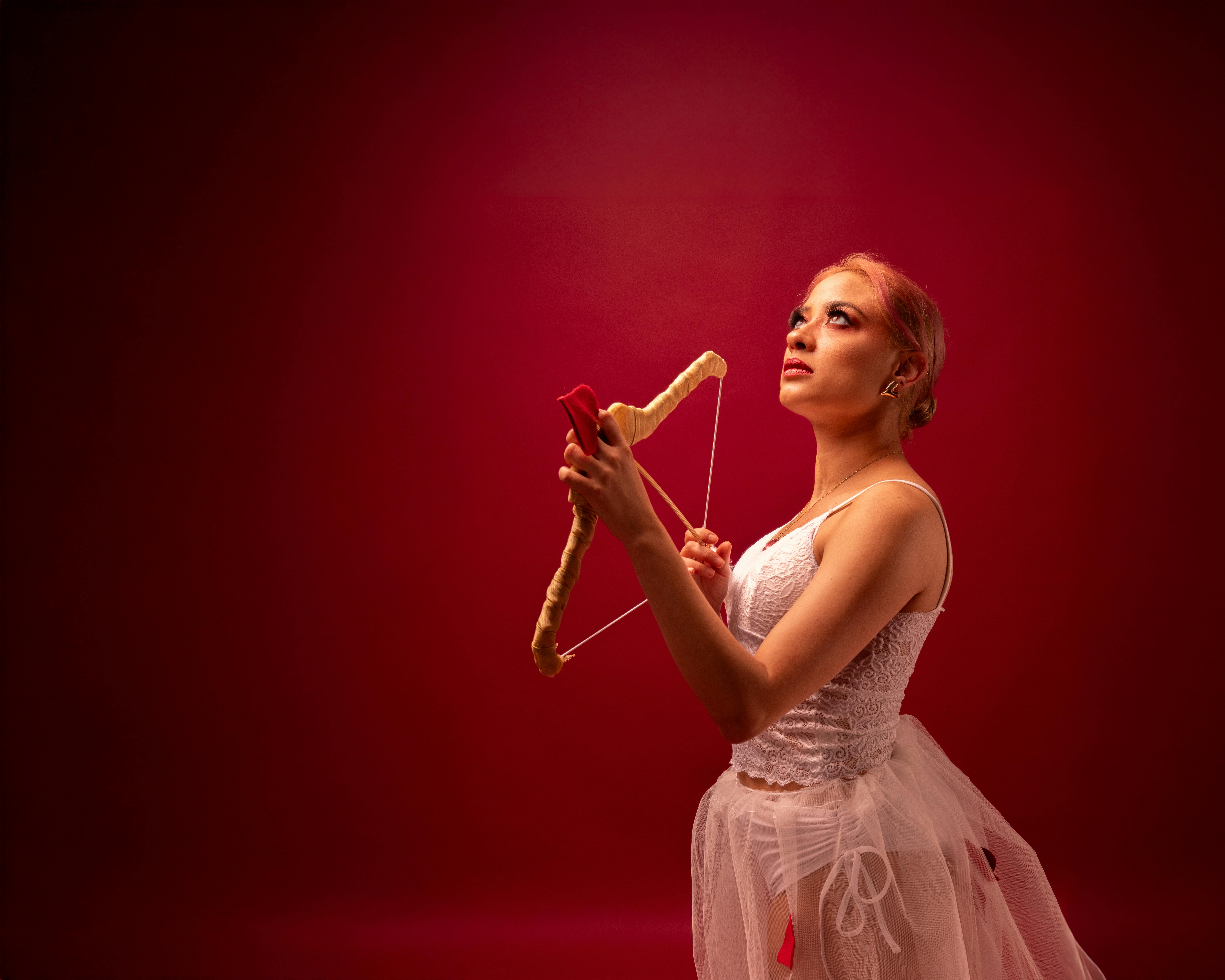 Ücretsiz Kırmızı bir fon önünde elinde yay tutan, aşk tanrısı temalı kostümlü bir balerin. Stok Fotoğraflar