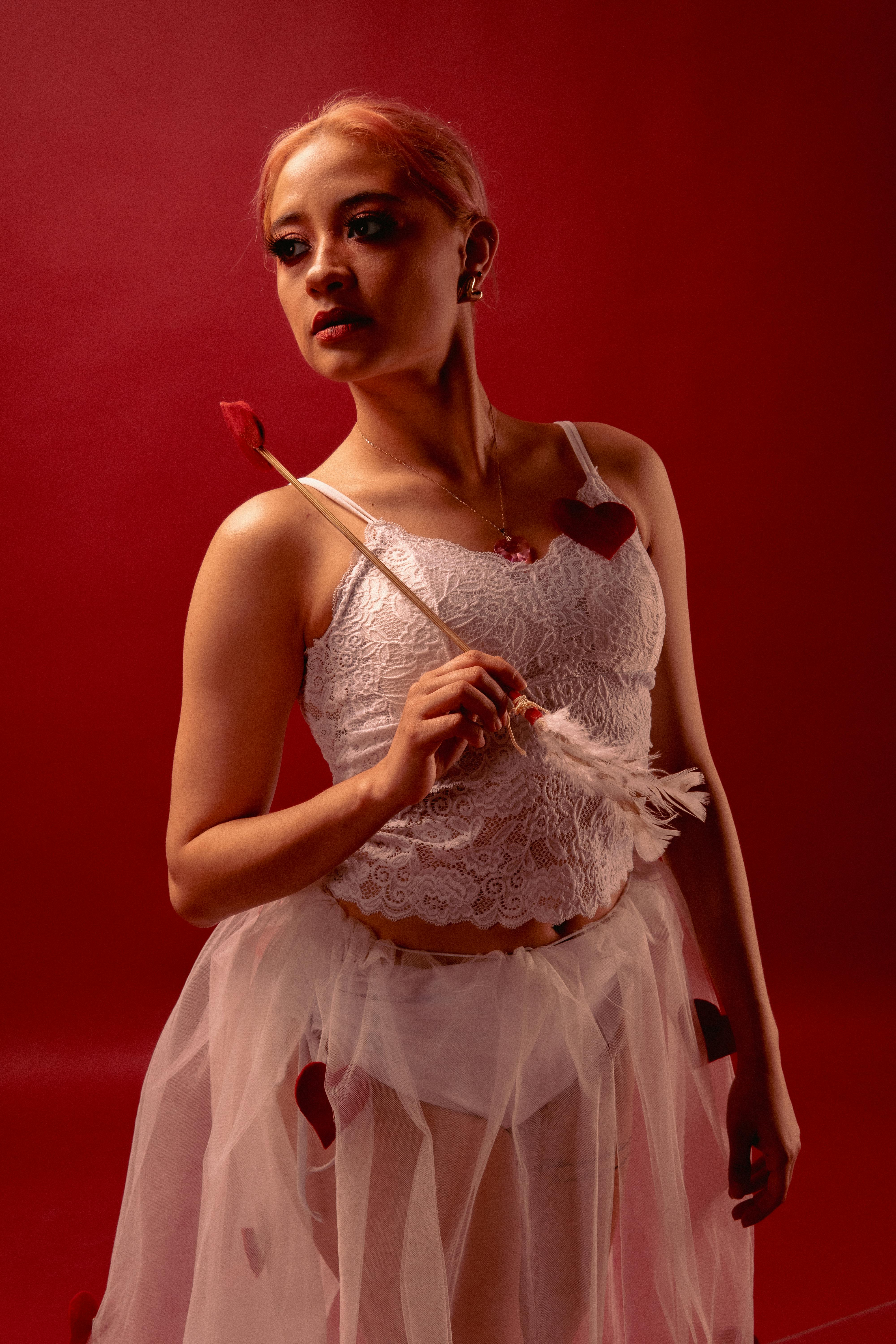 Ücretsiz Kırmızı fonda beyaz kostümle zarif bir şekilde poz veren bale dansçısı. Stok Fotoğraflar