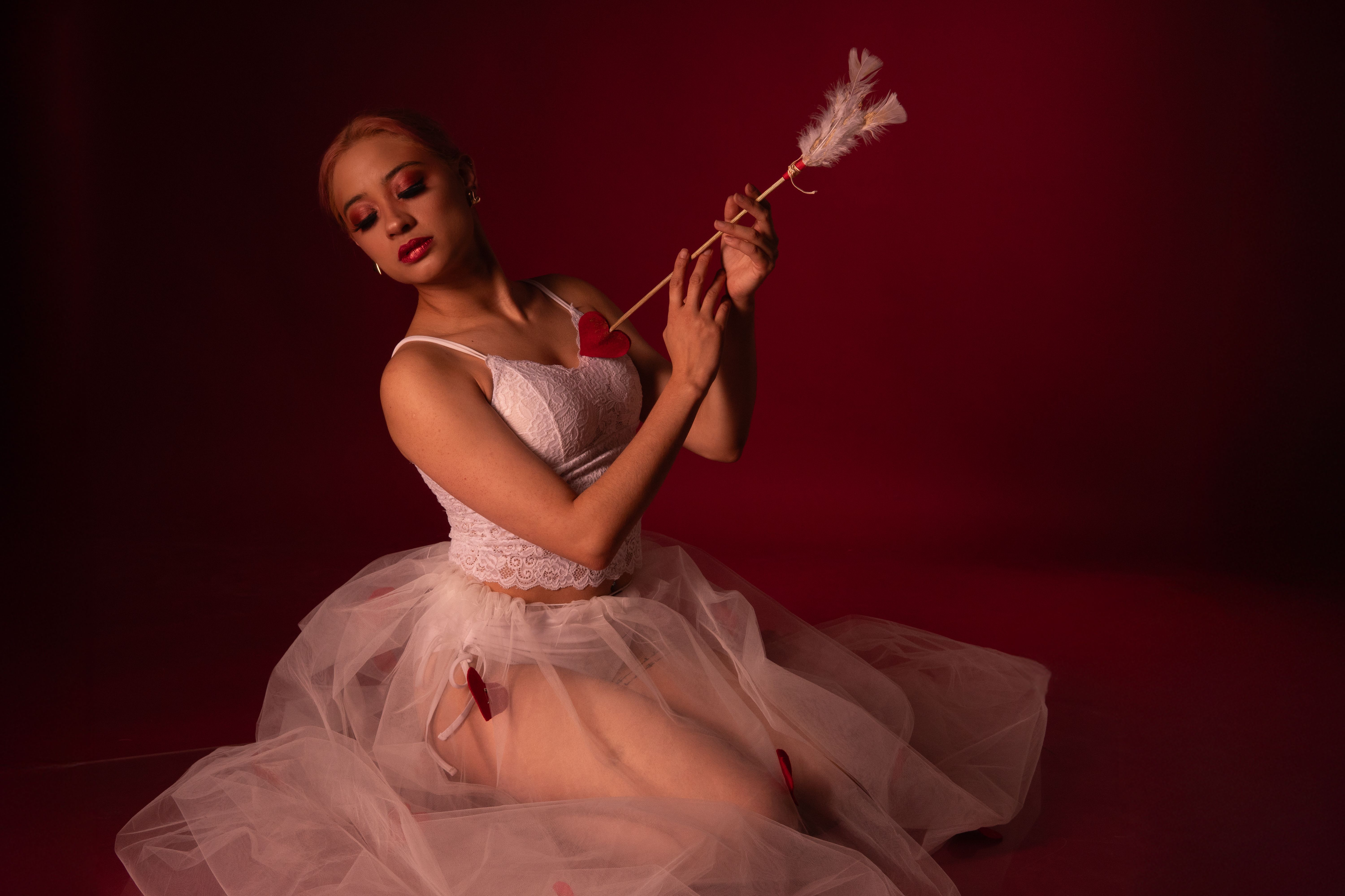 Une danseuse de ballet gracieuse dans un tutu blanc posant avec une flèche de Cupidon sur un fond rouge.