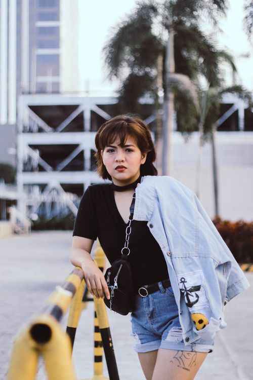 Free Casual portrait of a young woman standing outdoors with a city backdrop, exuding a stylish urban vibe. Stock Photo