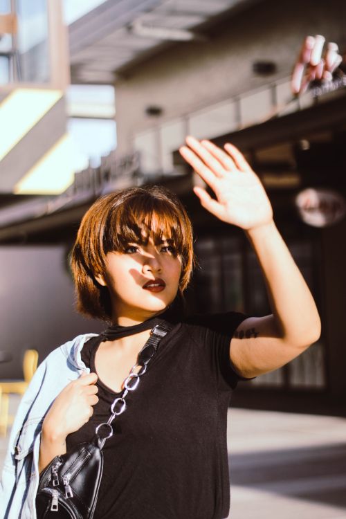 Free Young woman with short hair shielding eyes from sunlight with a hand gesture. Bright outdoor setting. Stock Photo