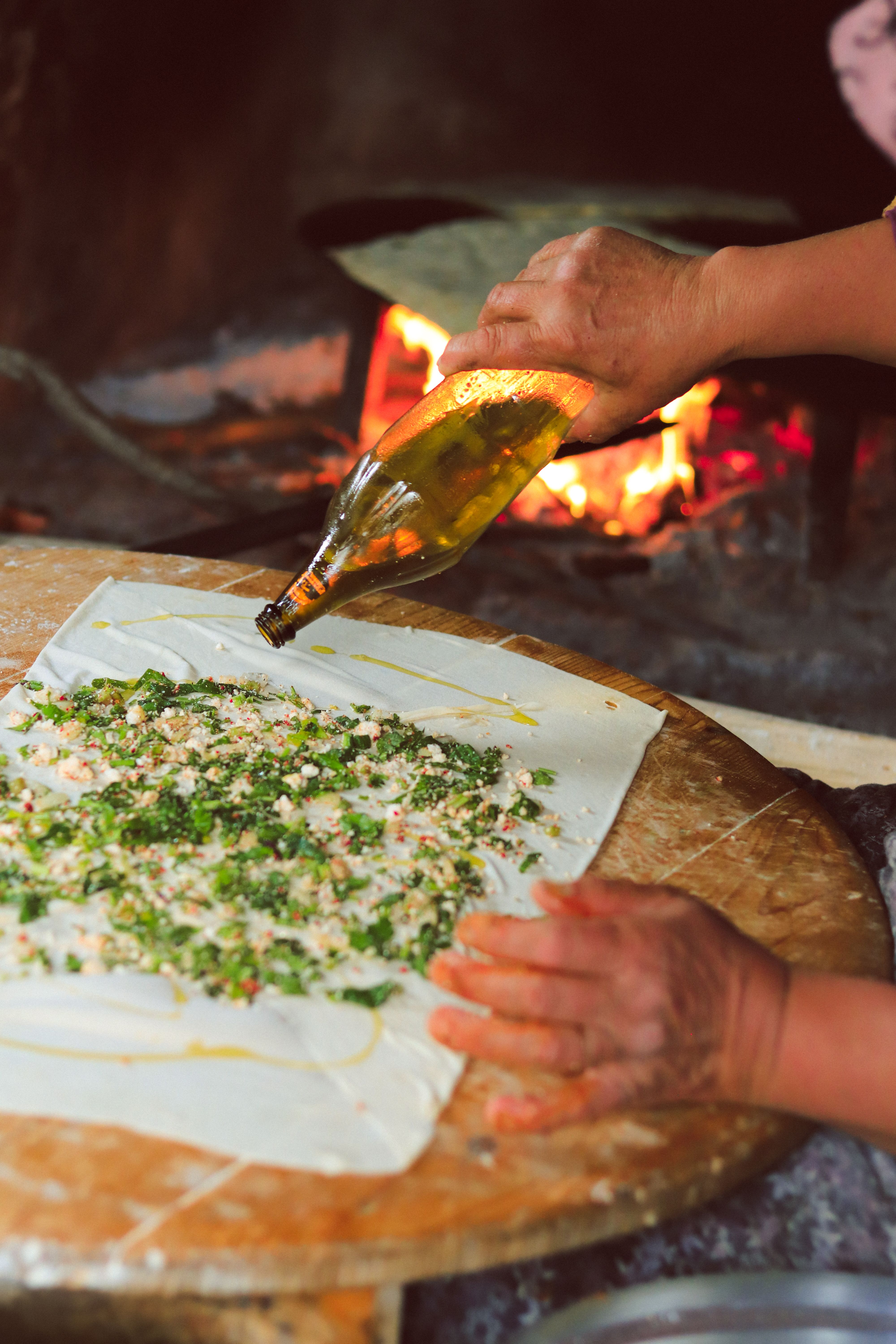 Hand preparing pastry on wooden board with ingredients near wood fire for authentic flavor.