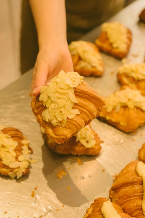 Free Hand picking fresh almond croissant from a tray in a bakery. Stock Photo