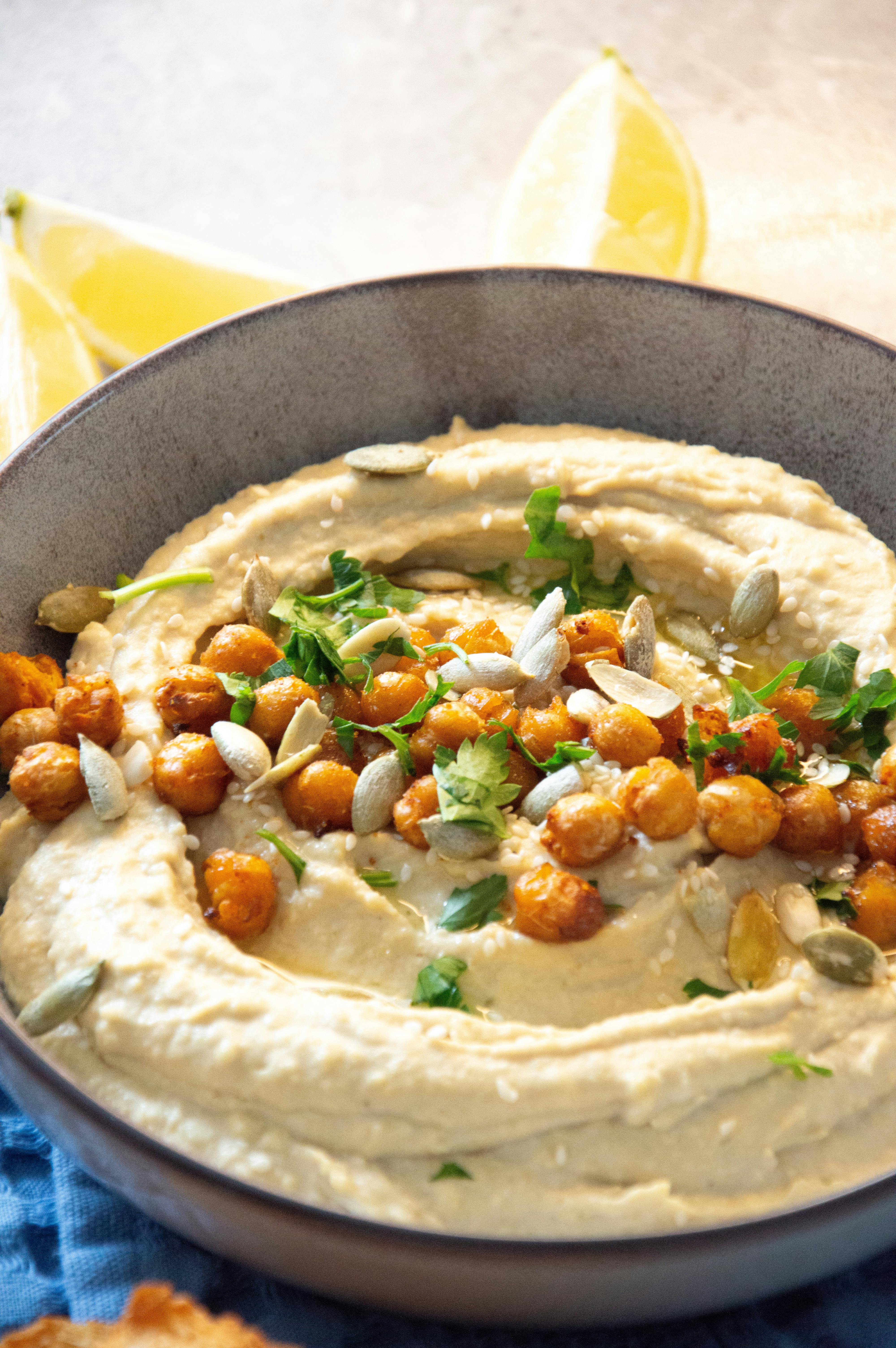 Dilara - Creamy hummus topped with roasted chickpeas, seeds, and fresh herbs, garnished with lemon slices.