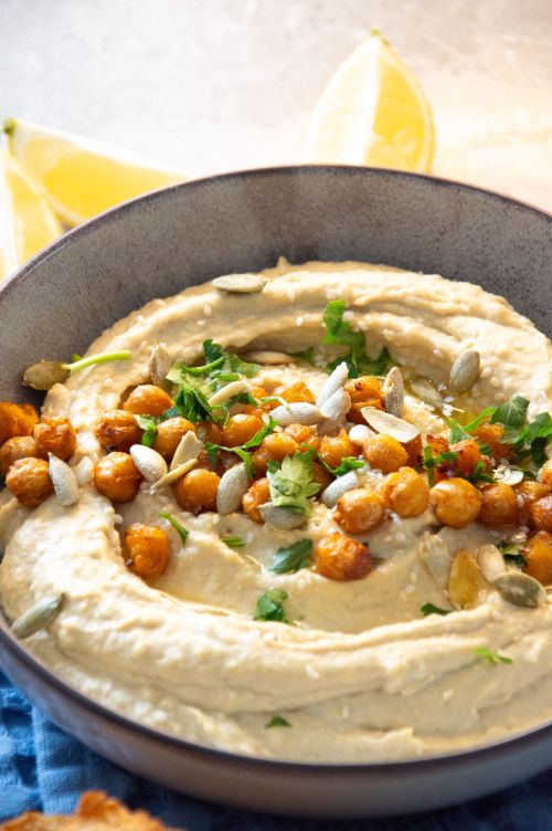 Free Creamy hummus topped with roasted chickpeas, seeds, and fresh herbs, garnished with lemon slices. Stock Photo