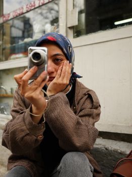 Woman in patterned scarf holding vintage camera on urban street.