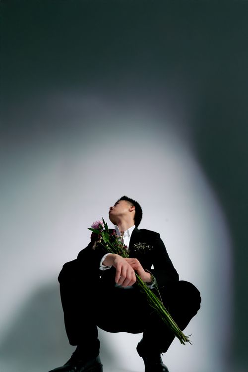 Free Artistic studio portrait of a man in a suit holding flowers, exuding creativity. Stock Photo