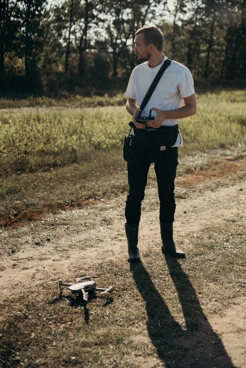 Free Man in casual attire controlling a drone in a sunny outdoor setting, emphasizing modern technology in nature. Stock Photo
