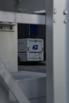 US mail delivery truck visible through urban metal framework on street.