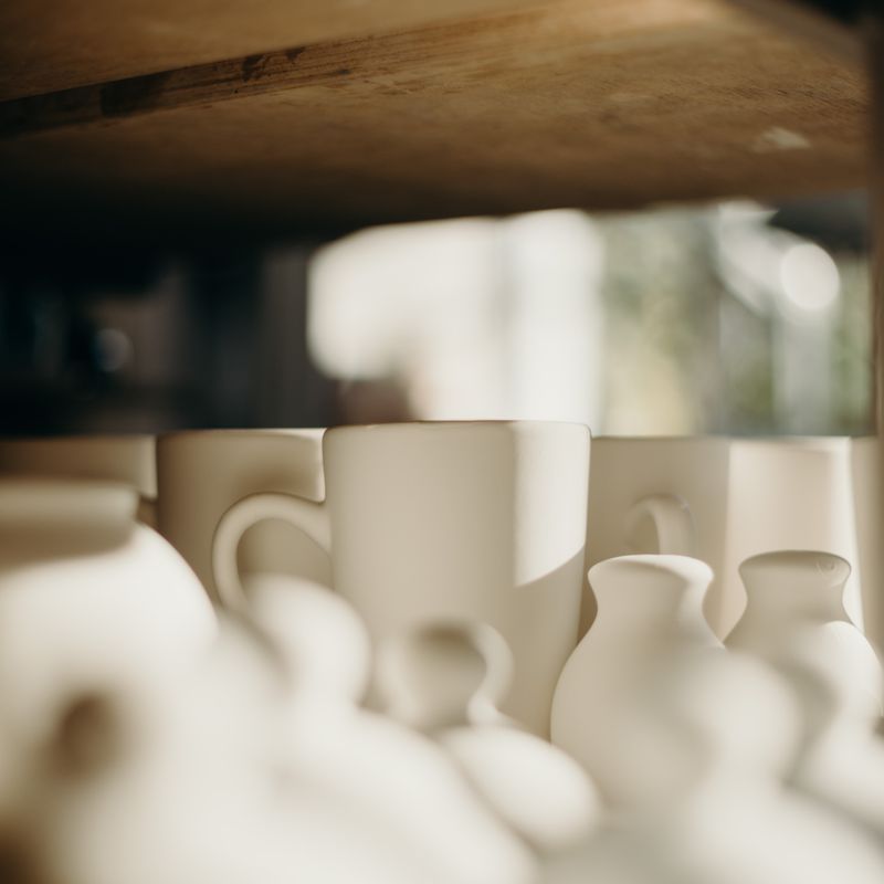 Handmade speckled mugs on a wooden shelf