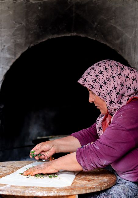 Woman crafting traditional flatbread with herbs in a rustic kitchen setting.