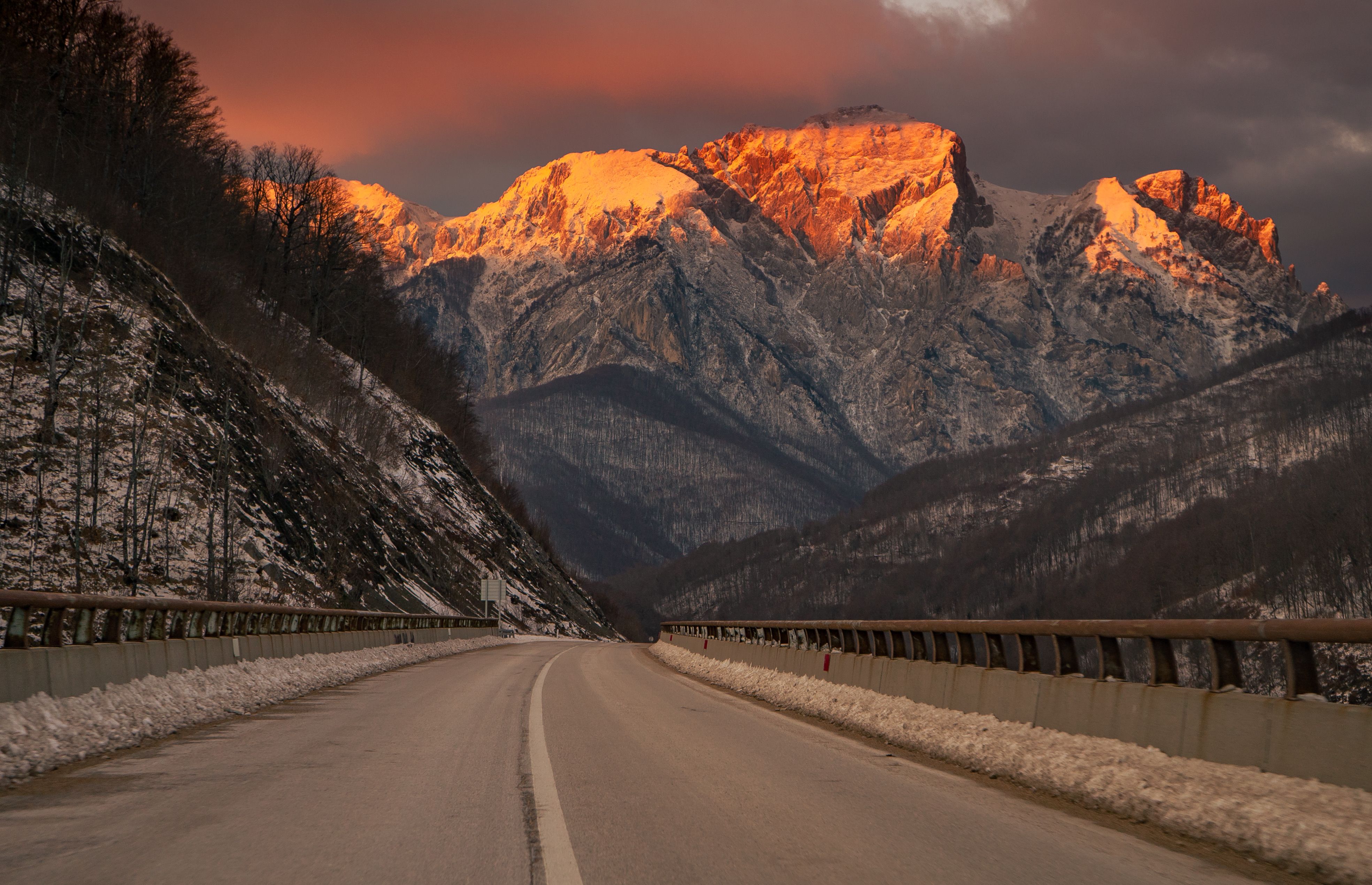 A road running towards a snow-covered massif lit by low sun