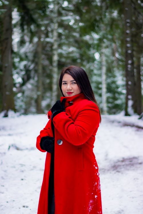 Free Asian woman in a striking red coat enjoying a snowy winter forest scene. Stock Photo