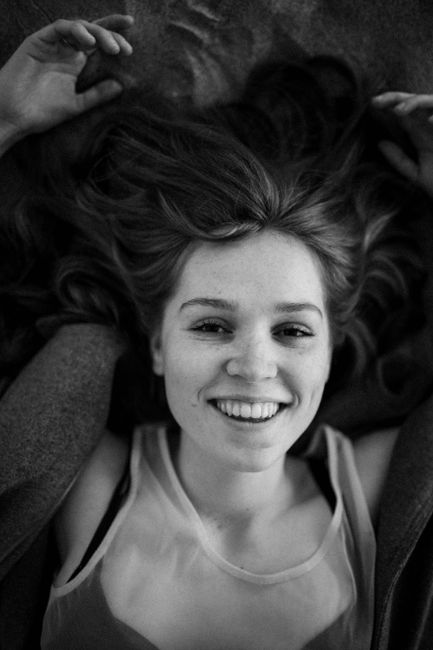 Black and white portrait of a smiling woman lying down with loose hair.