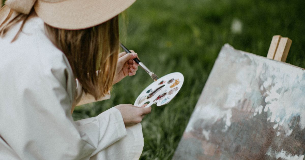 Woman painting outdoors with a palette and canvas in a sunlit garden setting