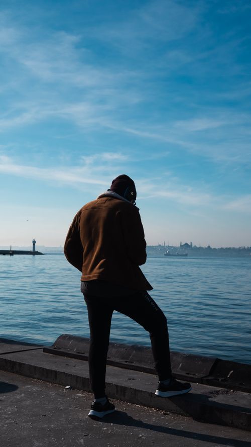 Free A person standing by a waterfront, gazing at the scenic view under a bright blue sky. Stock Photo